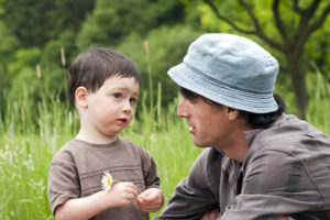 父亲和蹒跚学步的儿子在绿色的夏季草地上交谈。